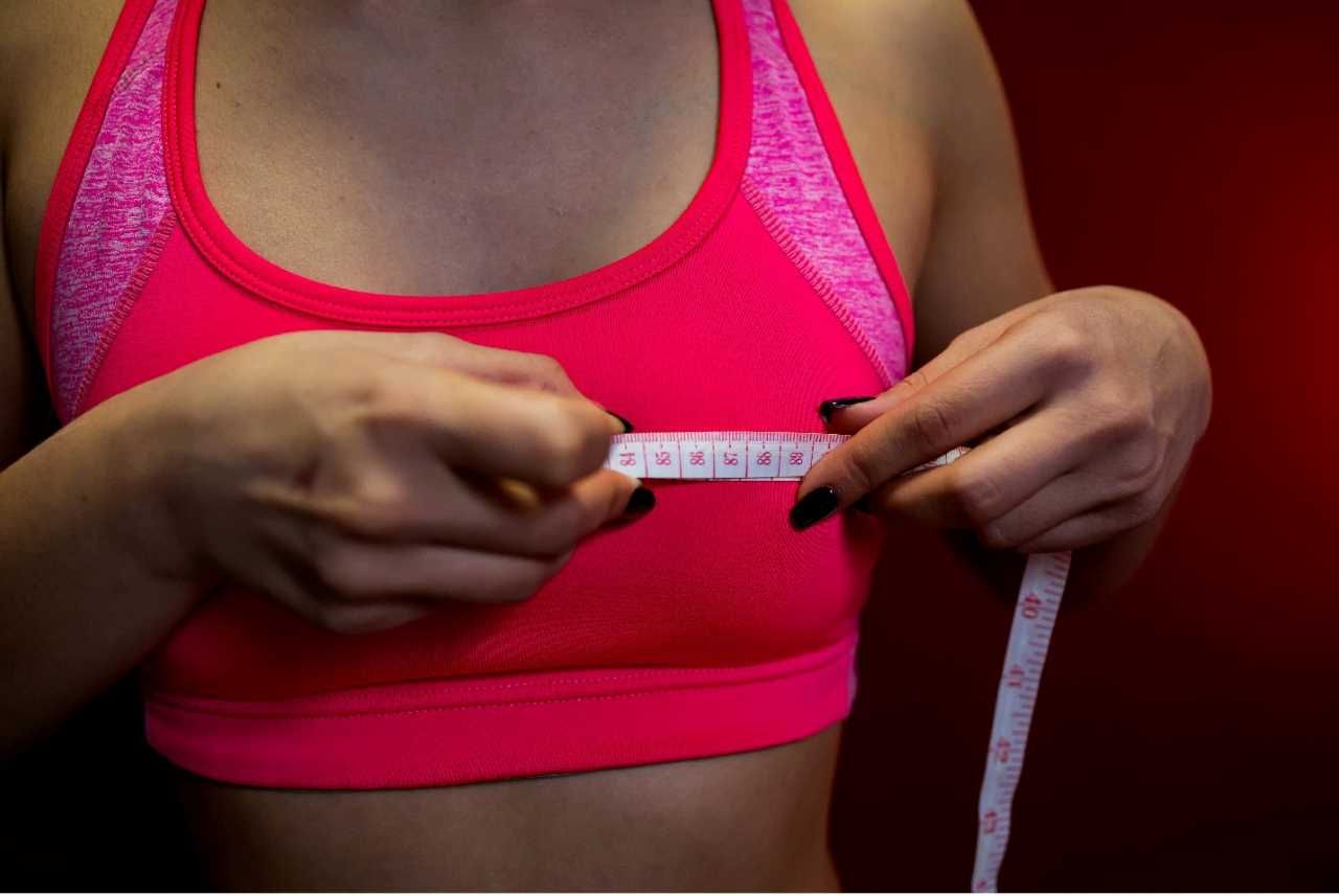 woman wearing red sports bra using measuring tape