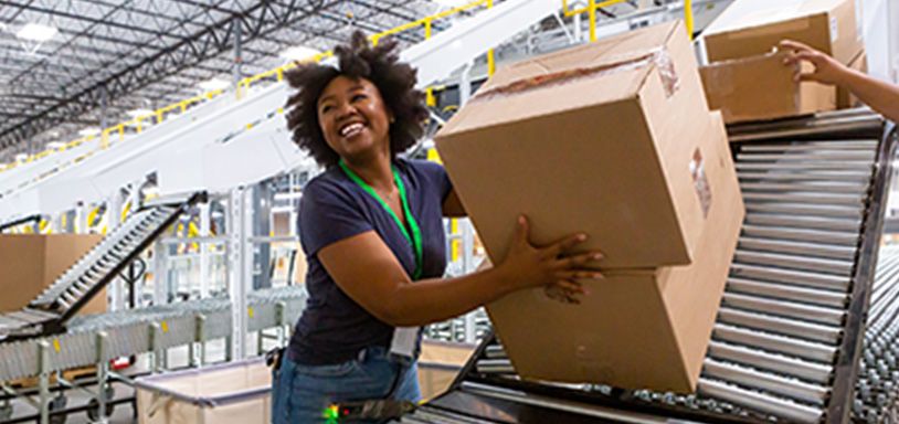 Smiling woman in warehouse taking boxes off an assembly line